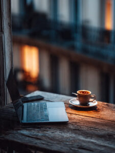 Laptop on rustic wooden table with coffee cup at dusk — symbolizing a solopreneur building one site that actually works.